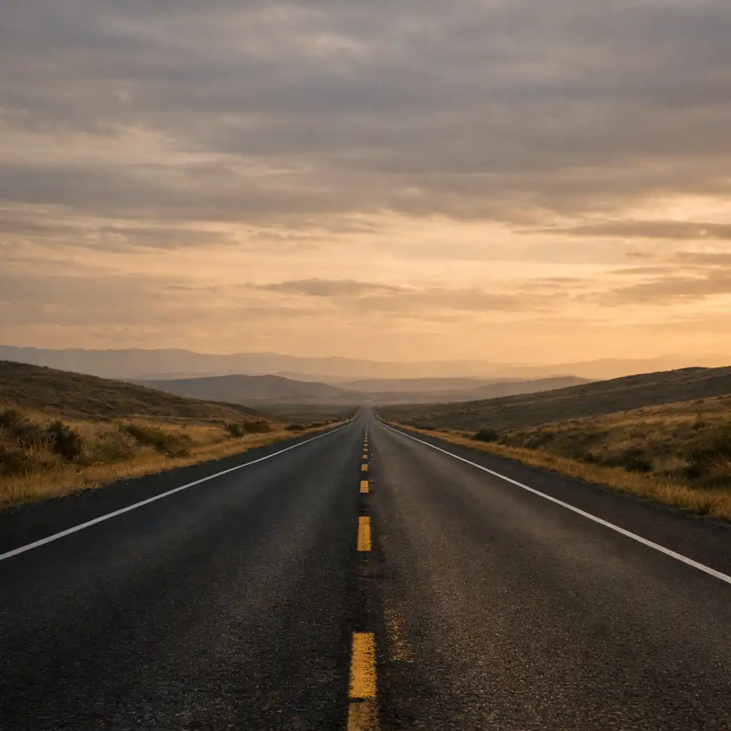 Empty asphalt route receding through low rolling terrain beneath a muted horizon